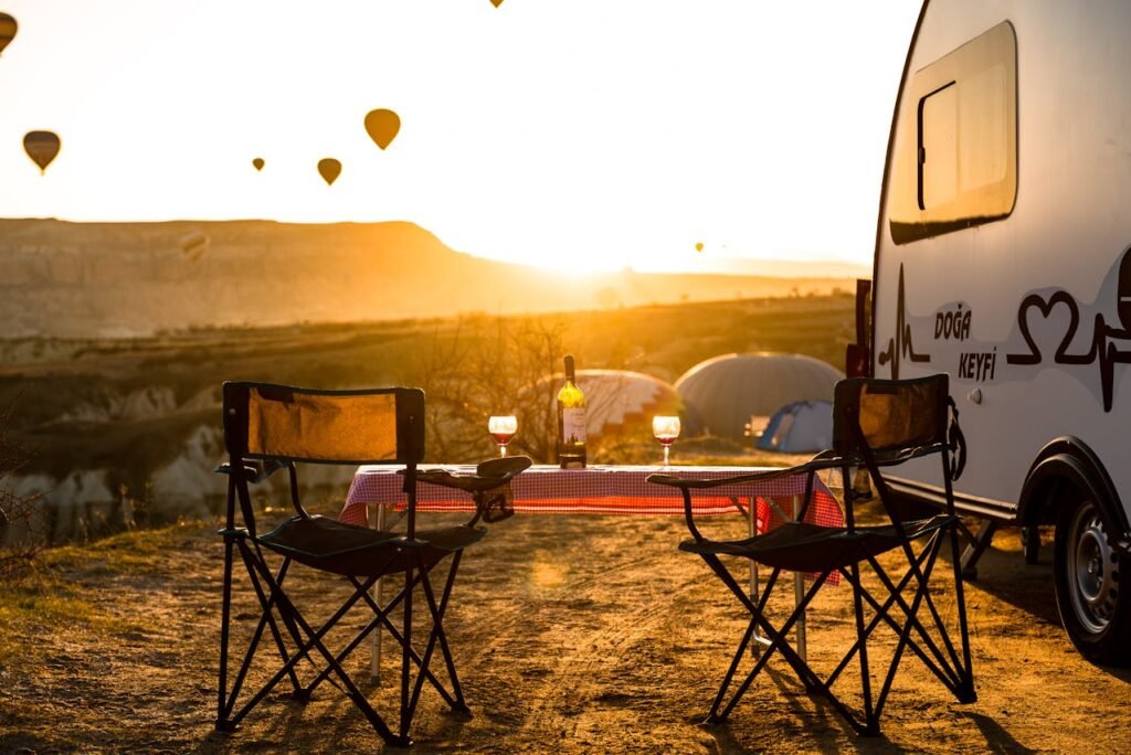 Klappstühle und Tisch mit Weingläsern neben einem Wohnwagen beim entspannten Campen.

