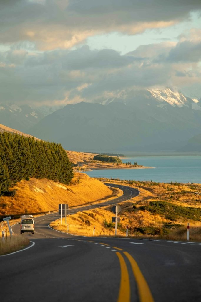 a-truck-driving-down-a-road-next-to-a-lake-4czc0qehmz4