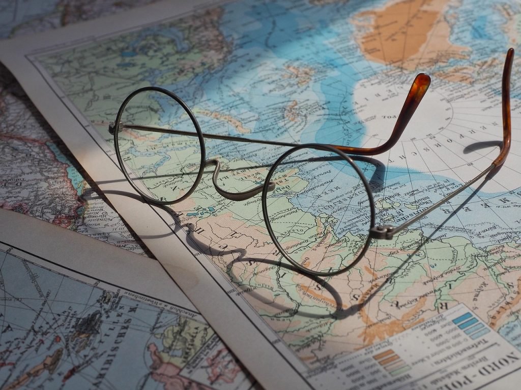 Eine Brille liegt auf einer Landkarte und einem Notizbuch. Symbolisiert die Reiseplanung.