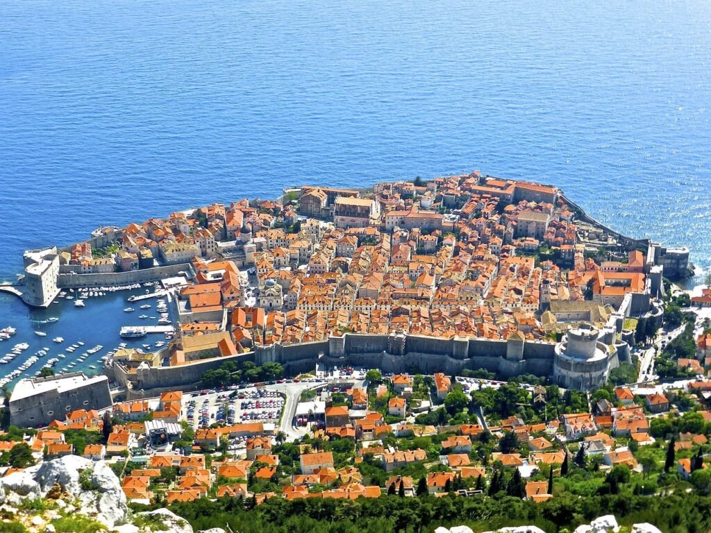 Blick auf die historische Altstadt von Dubrovnik, umgeben von den imposanten mittelalterlichen Stadtmauern, die sich bis ins Meer erstrecken.