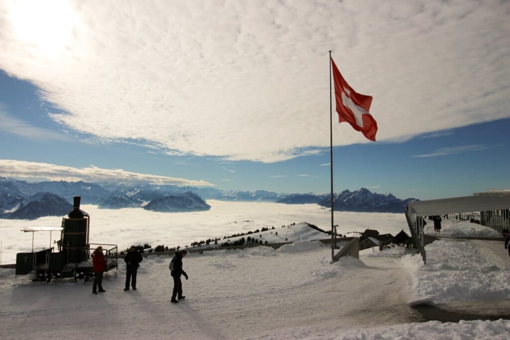 Silhouette von drei Personen auf dem Rigi Kulm mit der Schweizer Flagge, Symbol für ein Wohnmobil-Abenteuer in den Schweizer AlpenDie 10 schönsten Wohnmobil Routen in der Schweiz